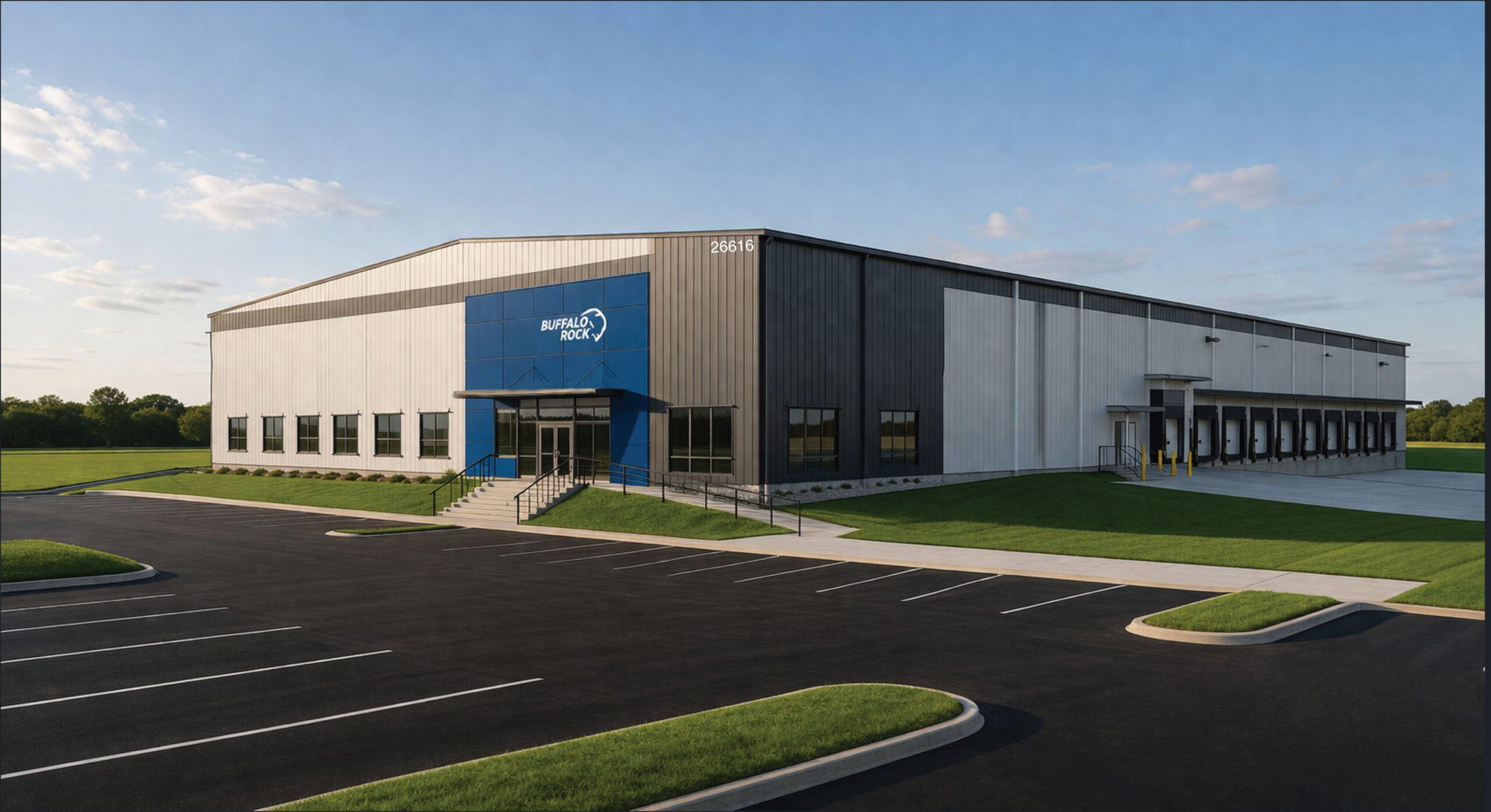 A large, modern industrial warehouse with a blue entrance and a sign reading BUFFALO ROCK stands in Foley’s newly acquired industrial park, thanks to a $3.3 million SEEDS Grant. It’s surrounded by grass, trees, and a mostly empty parking lot under partly cloudy skies.