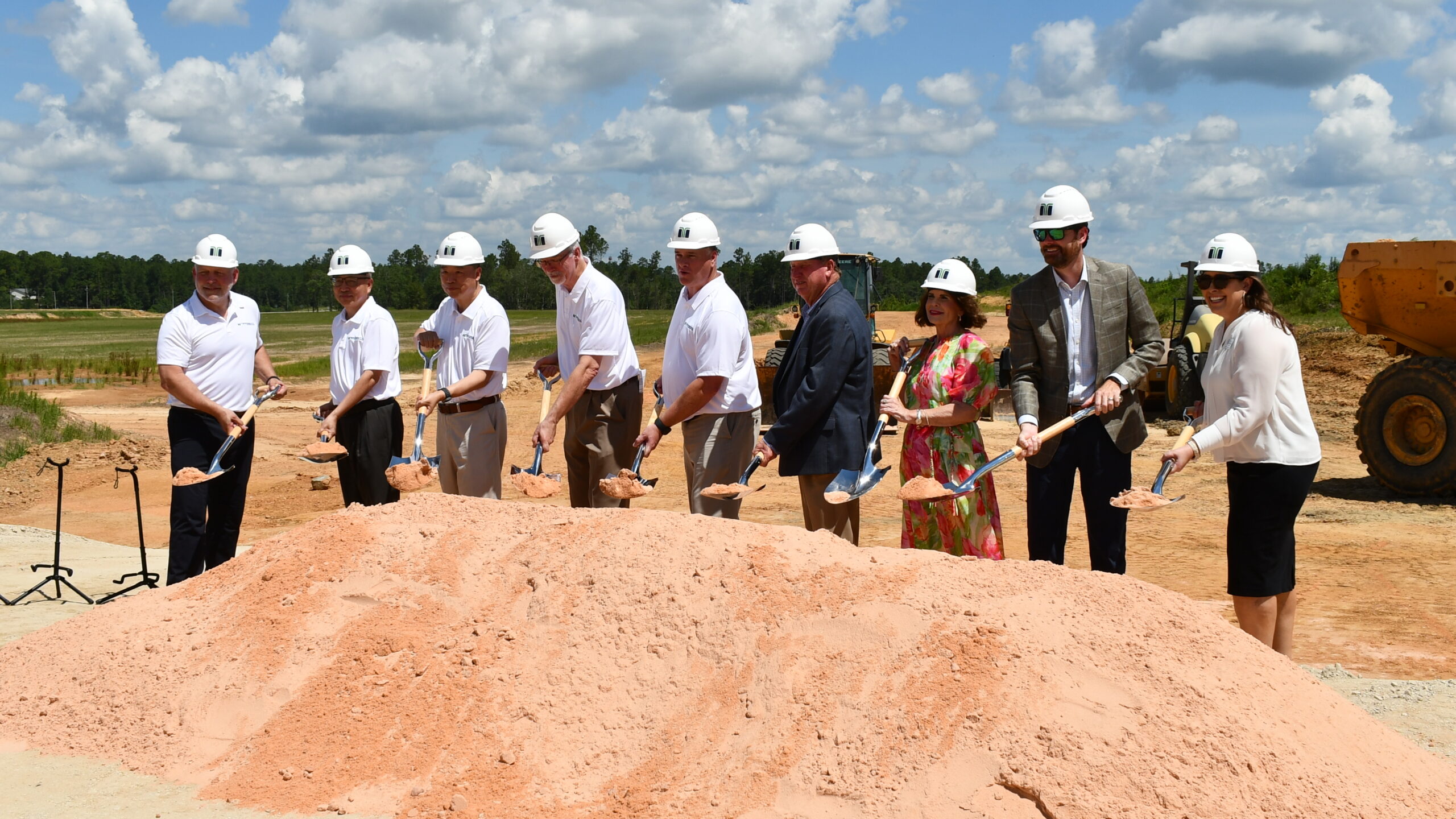 Eight people in hard hats stand in a row, holding shovels and posing for a groundbreaking ceremony at a construction site with a mound of dirt in front of them, as Infirmary Health invests in a new facility at Spanish Fort Town Center.