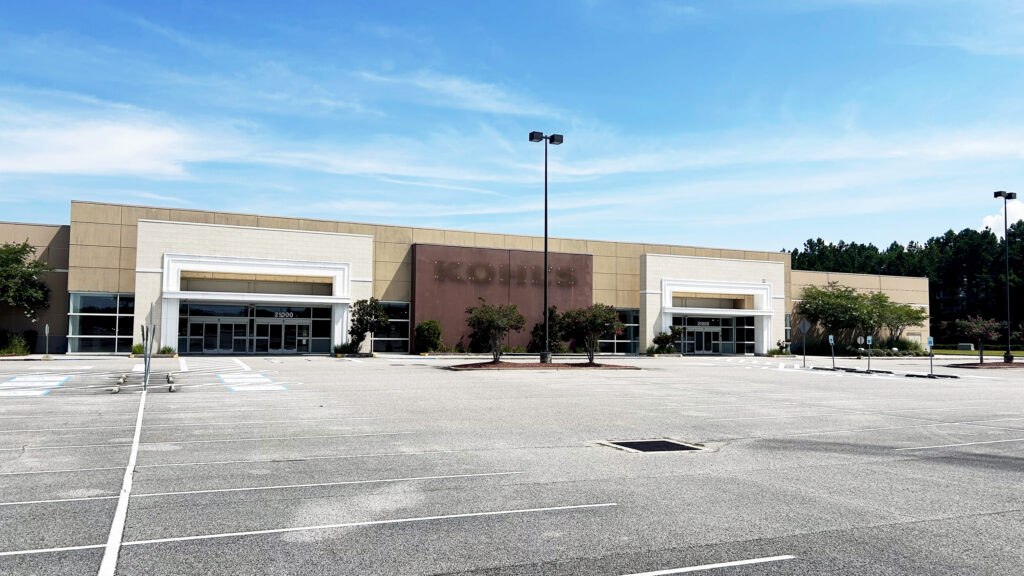 An empty parking lot in front of a large, closed Kohls store on a sunny day, with trees and blue sky in the background—future site as Buffalo Rock Company is expanding to Loxley.
